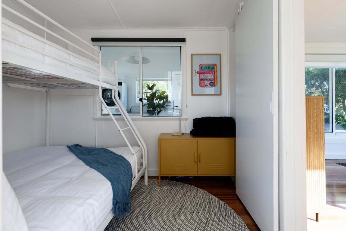 Un dormitorio con literas, un armario pequeño, una ventana con vistas y un cuadro en la pared.