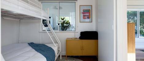 Un dormitorio con literas, un armario pequeño, una ventana con vistas y un cuadro en la pared.