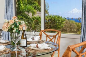 Une table à manger dressée pour deux personnes, avec vue sur un paysage tropical grâce à de grandes fenêtres.