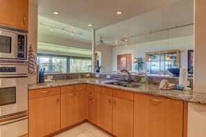 A modern kitchen with granite countertops, wooden cabinets, a stainless steel sink, and a built-in oven. - Kapalua Ridge | Ocean View 5 BR, Sleeps 14 | Car Incl. w/ 6+ Nights | KRV ML-3948 by KBM (Lahaina)
