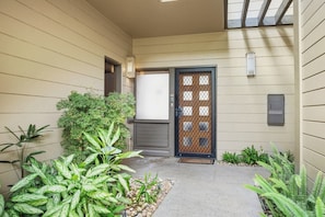A residential building with a front door, a small garden area with various plants, and a mailbox. - Kapalua Ridge | Ocean View 5 BR, Sleeps 14 | Car Incl. w/ 6+ Nights | KRV ML-3948 by KBM (Lahaina)