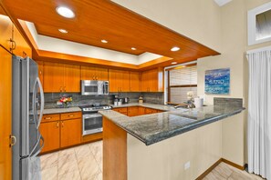 Una cocina moderna con armarios de madera, encimeras de granito, un refrigerador de acero inoxidable y un microondas.