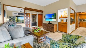 Ein Wohnzimmer mit Sofa, Couchtisch, Fernseher und Küchenbereich mit Holzausbau.