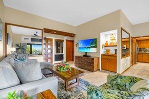 Sala de estar con sofá, mesa de centro, televisor y zona de cocina con armarios de madera.