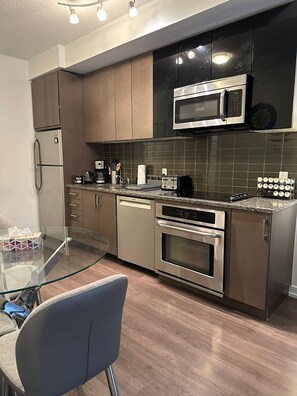 Eine moderne Küche mit Edelstahlgeräten, einem Glastisch und einer dunkel gefliesten Spritzschutzwand.