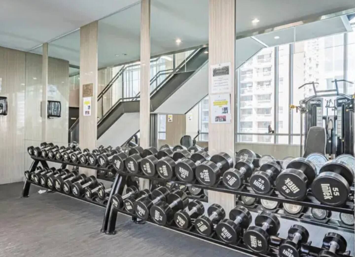A gym with weightlifting equipment, a staircase, and large windows.