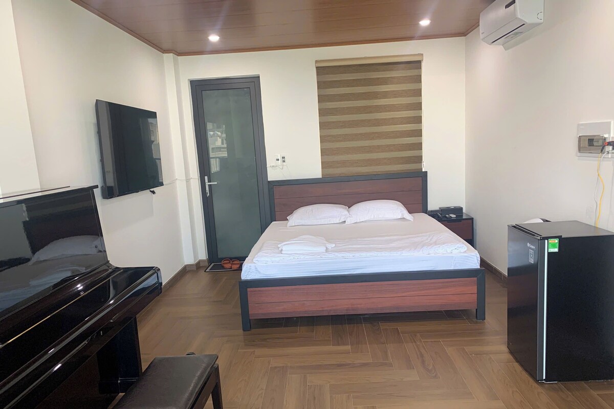 Ein Schlafzimmer mit einem Bett, einem Fernseher, einem Kühlschrank, einem Klavier und einer Bank.