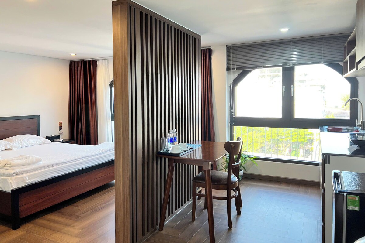 Ein Hotelzimmer mit Bett, Schreibtisch mit Stuhl, einem Fenster mit Aussicht und einer Küchenzeile.
