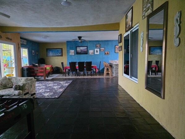 Una habitación con una mesa de fútbol de mesa, un comedor con sillas y una mesa, y un ventilador de techo.