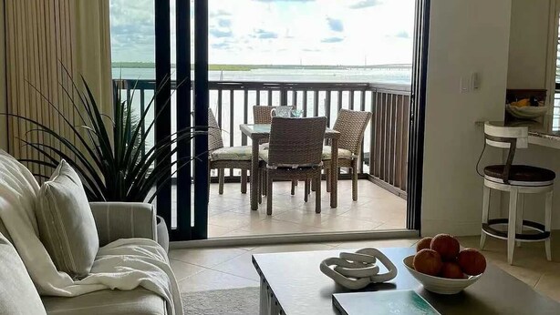 Een kamer met een bank, een eettafel met stoelen, een balkon met uitzicht op zee en een plafondventilator.