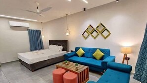 Ein modernes Hotelzimmer mit einem Bett, einem blauen Sofa, roten Hocker, einem Holztisch und dekorativen Wandspiegeln.