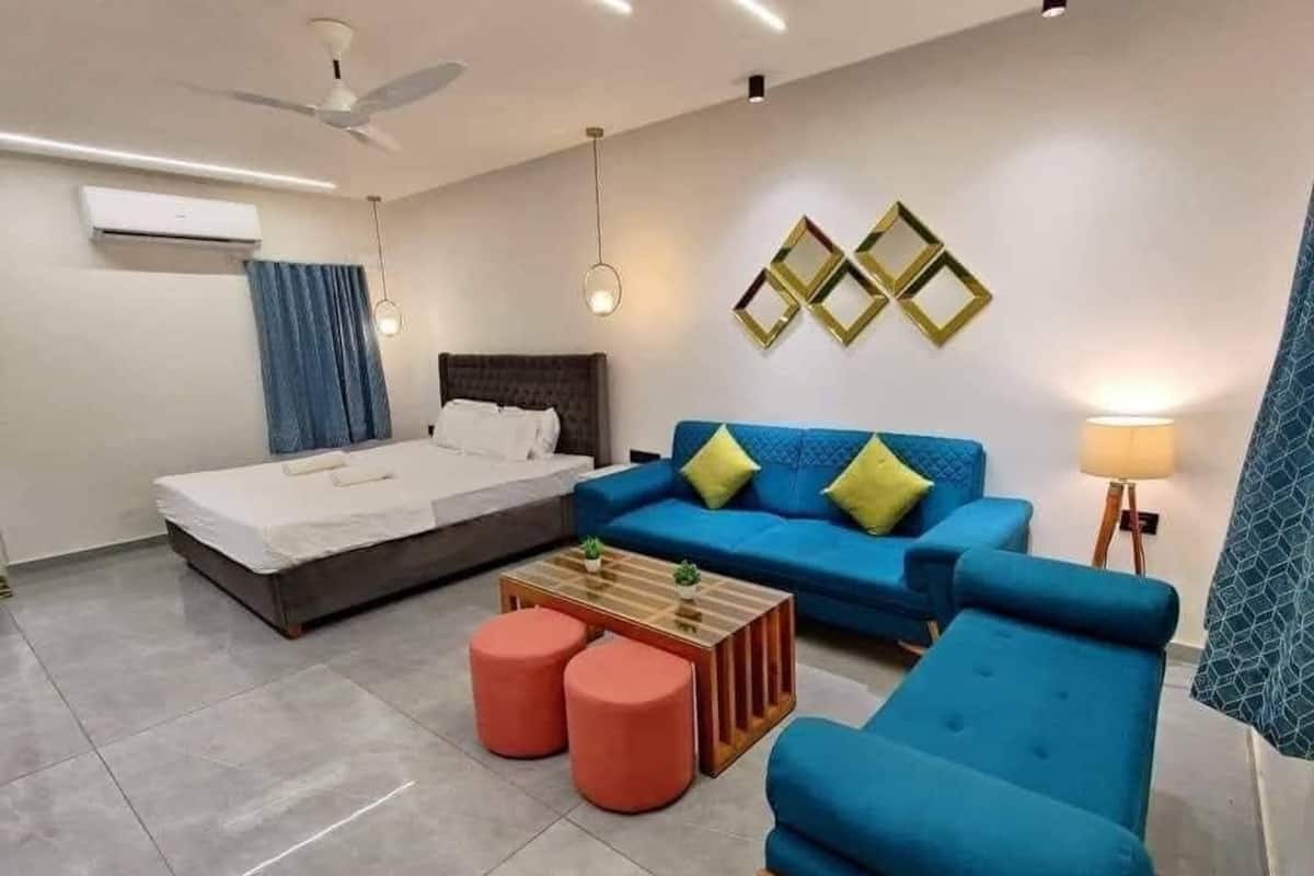A modern hotel room with a bed, blue sofa, red ottomans, a wooden coffee table, and decorative wall mirrors.