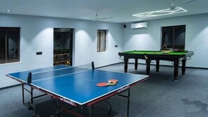 Ein Zimmer mit Tischtennisplatte, Billardtisch und Deckenventilator.