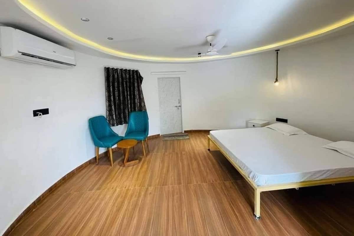 A room with a bed, a chair, an air conditioning unit, a ceiling fan, and a door.