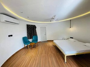 Ein Zimmer mit einem Bett, einem Sessel, einer Klimaanlage, einem Deckenventilator und einer Tür.