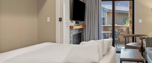 Une chambre d’hôtel comprenant un lit, un téléviseur à écran plat, une cheminée, un balcon avec coin salon extérieur et un espace repas.