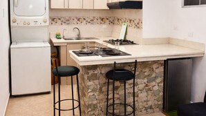 A compact kitchen with a built-in stove, a washing machine, and a small dining area with stools. - Nova Suite : Modern and cozy in the center of Guayaquil (Guayaquil)