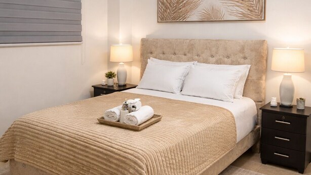 A neatly arranged bedroom with a large bed, two bedside tables with lamps, a wall-mounted artwork, and a window with blinds. - Nova Suite : Modern and cozy in the center of Guayaquil (Guayaquil)