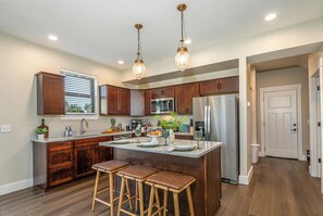 A modern kitchen with wooden cabinets, stainless steel appliances, and a central island with stools. - Brand New Home! Hot Tub Massage Chair Game Room, Dog Friendly, Fun for all ages! (Galena)