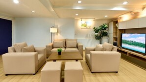A modern living room with beige sofas, a coffee table, a TV, and a plant. - TEN-Place Srinakarin (Bangkok)