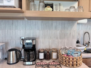 A kitchen with a coffee maker, jars, and a basket of snacks.