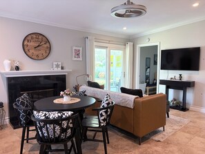 A living room with a fireplace, a dining table with chairs, a sofa, a television, and a clock on the wall.