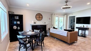 Een eetgedeelte met een ronde tafel en stoelen, een open haard, een klok en een televisie aan de muur.