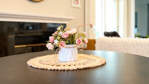 Een tafel met een vaas roze bloemen, een klok aan de muur en een open haard.