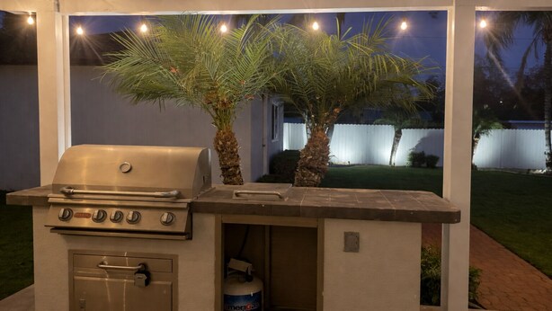 Een buitenbarbecue met ingebouwde oven, een propaantank en een palmboom.