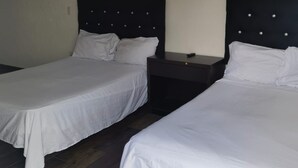 Twee eenpersoonsbedden met donkere hoofdborden en witte beddengoed, een klein nachtkastje met een lamp, en een donkere houten vloer.