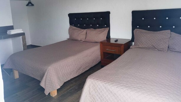 Une chambre avec deux lits, chacun doté d’une tête de lit, d’une table de chevet et d’un porte-serviettes mural.