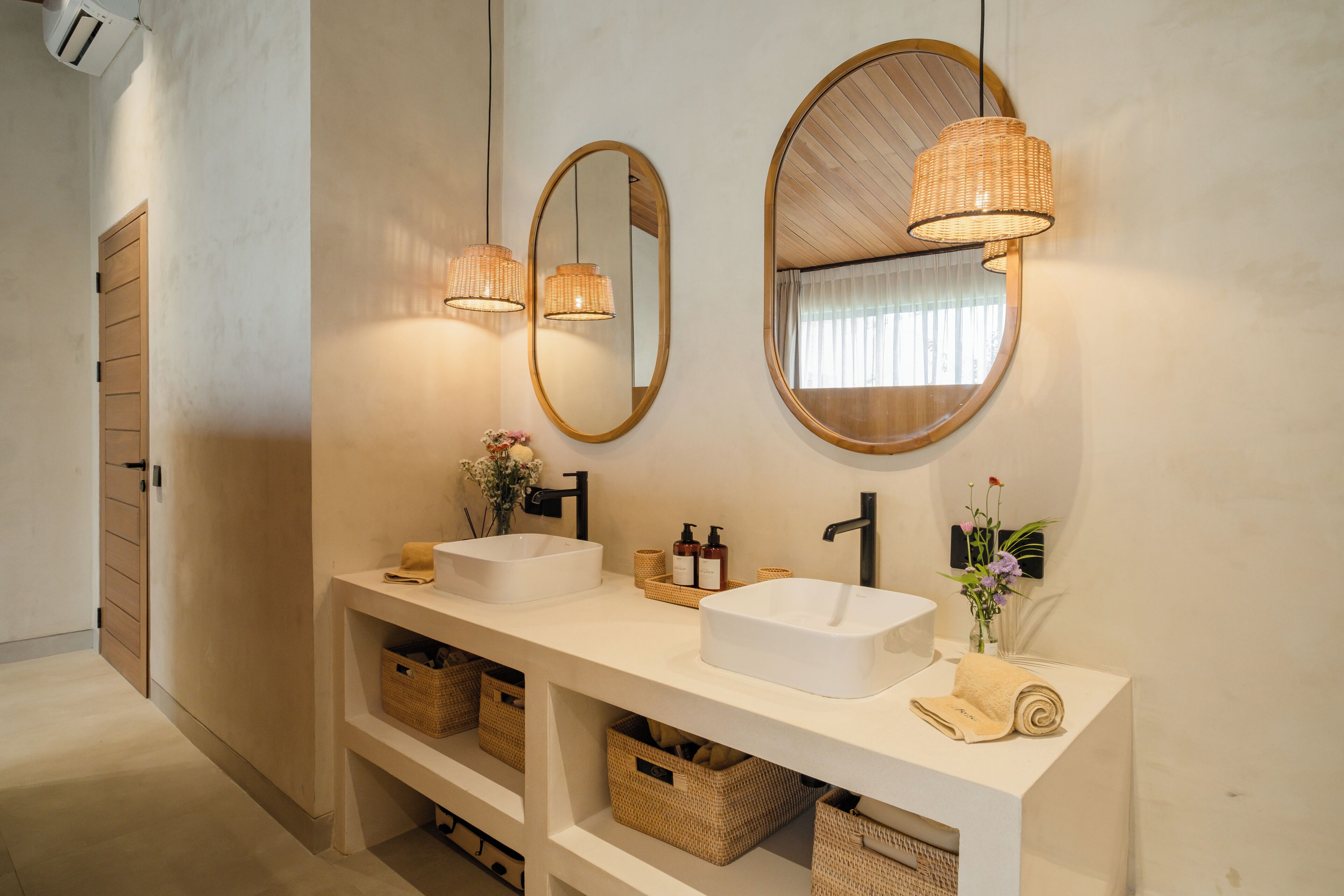 A bathroom with two sinks, a mirror, and wicker lamps.