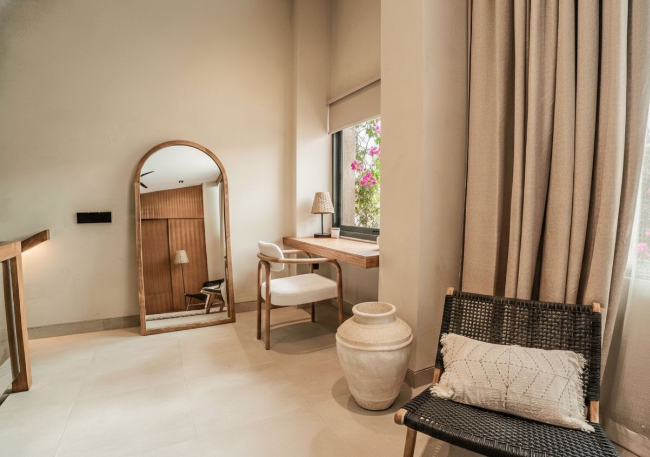 Une pièce avec un miroir, un bureau, une chaise, un grand vase et une fenêtre avec des rideaux.