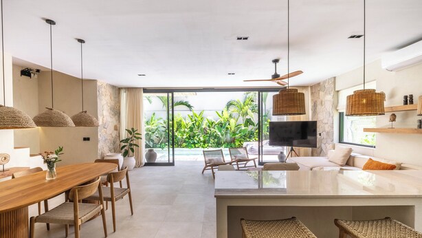 A modern kitchen with a central island, dining area with chairs, and a large window overlooking greenery. - La Brava  (Pecatu)