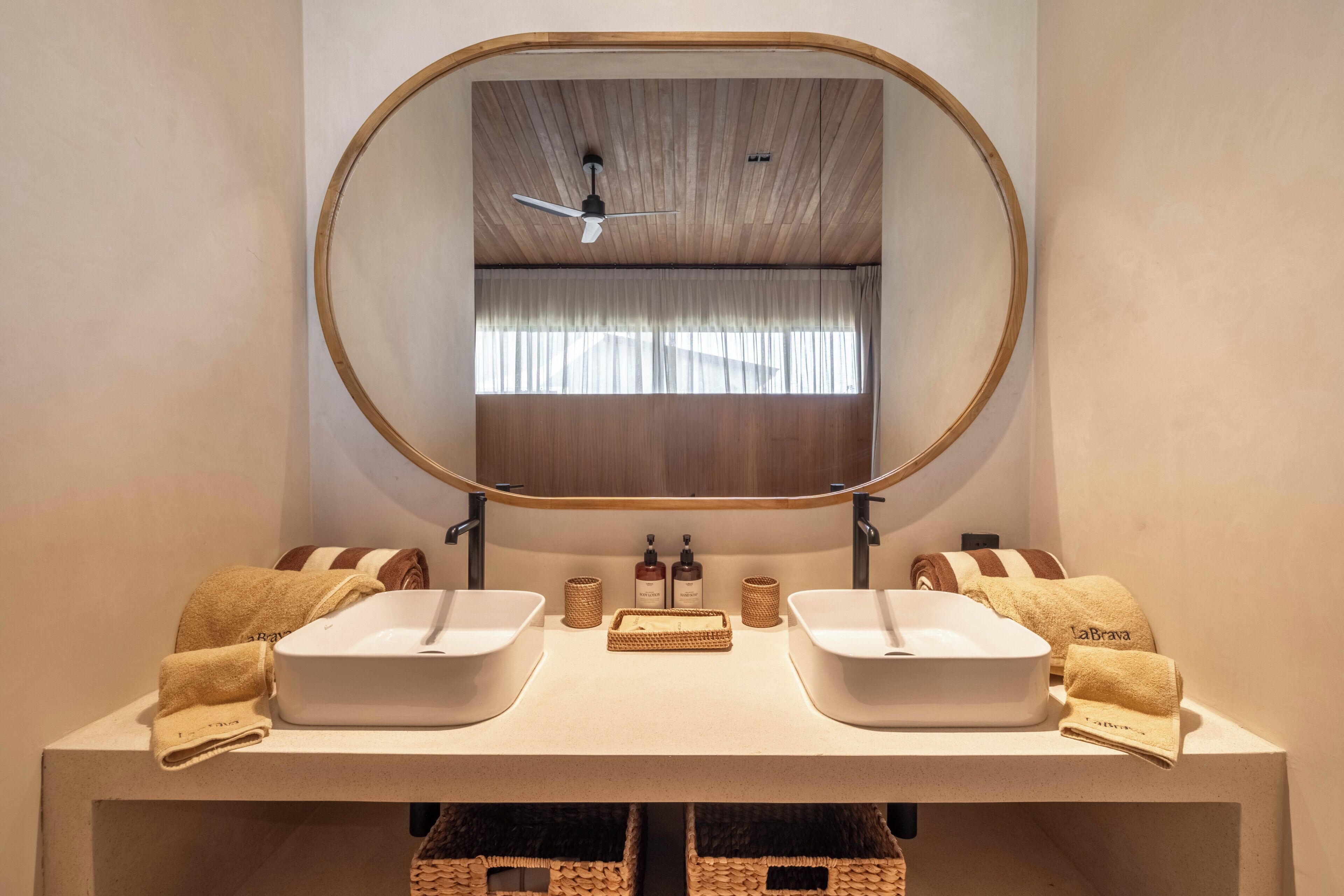 A bathroom with a wooden ceiling, a large oval mirror, two sinks, and towels.