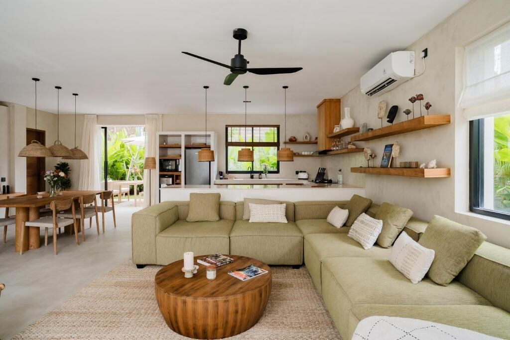 A modern living room with a large sectional sofa, a wooden coffee table, pendant lights, and a ceiling fan.