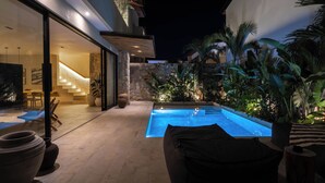 A modern outdoor pool area with stone walls, potted plants, and a well-lit interior. - La Brava  (Pecatu)