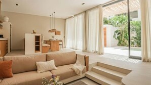 A modern living room with a sofa, a dining area, and a staircase leading to an outdoor area with plants. - La Brava  (Pecatu)