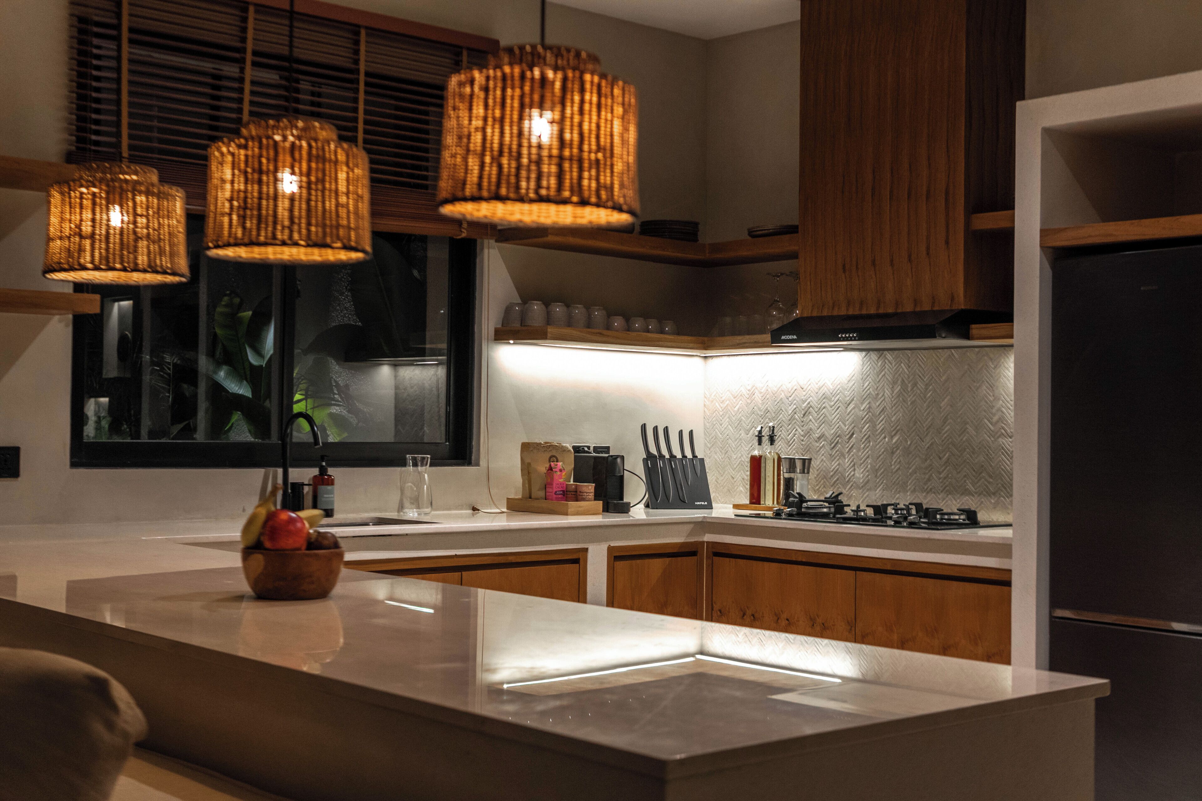 A modern kitchen with a central island, wooden cabinets, and three wicker pendant lights.