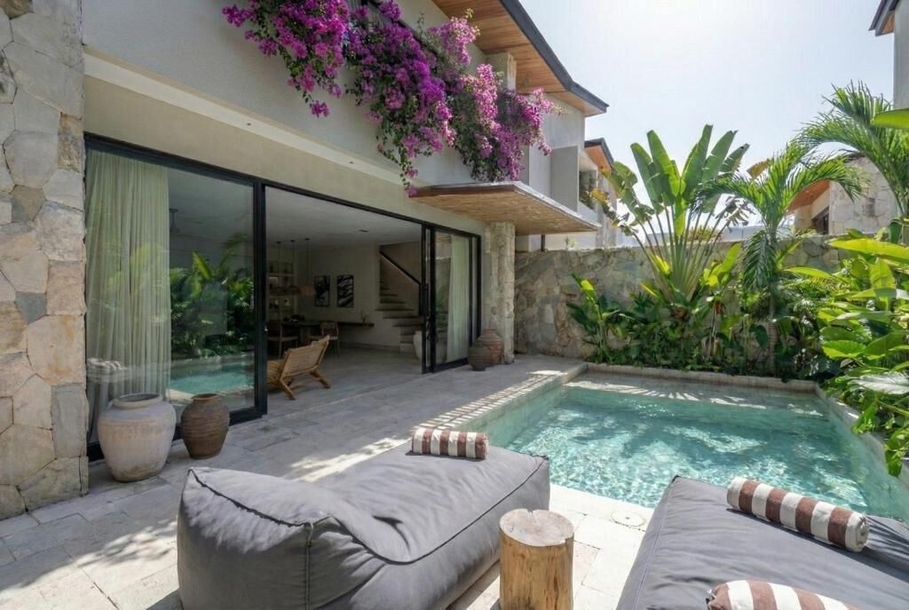 Una casa moderna con piscina, mobiliario de exterior y abundante vegetación.