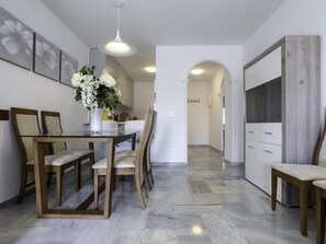 A modern kitchen with a dining table, chairs, a vase of flowers, and a TV. - Sunstay Sirius Flat II Mijas (Mijas)