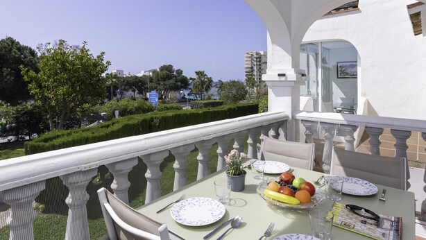 Un balcón con una mesa lista para comer, una planta en maceta y vistas despejadas del entorno, con vegetación y edificios.