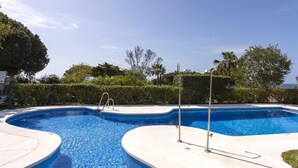 Una piscina de diseño curvo, rodeada por una solana de hormigón y bordeada de vegetación.