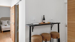 A modern room with a bed, a dining table with a bottle, glasses, and food, and two wicker stools. - TheBlueStay 261 - Stunning Designer Apt - Paris 15 (Paris)