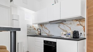 A compact kitchen with white cabinets, a marble backsplash, a black countertop, a built-in oven, and a coffee maker. - TheBlueStay 261 - Stunning Designer Apt - Paris 15 (Paris)