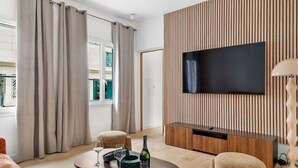 A modern living room with a flat-screen TV, a wooden panel wall, a round coffee table with wine glasses and a bottle, and a sofa. - TheBlueStay 261 - Stunning Designer Apt - Paris 15 (Paris)