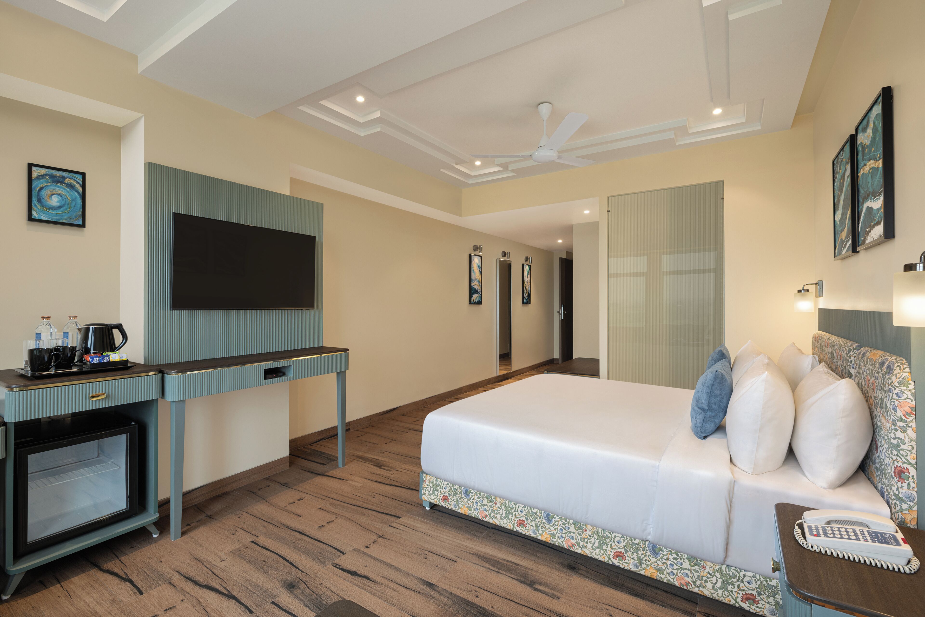 A hotel room with a bed, a desk with a flat-screen TV, a coffee maker, and a telephone.