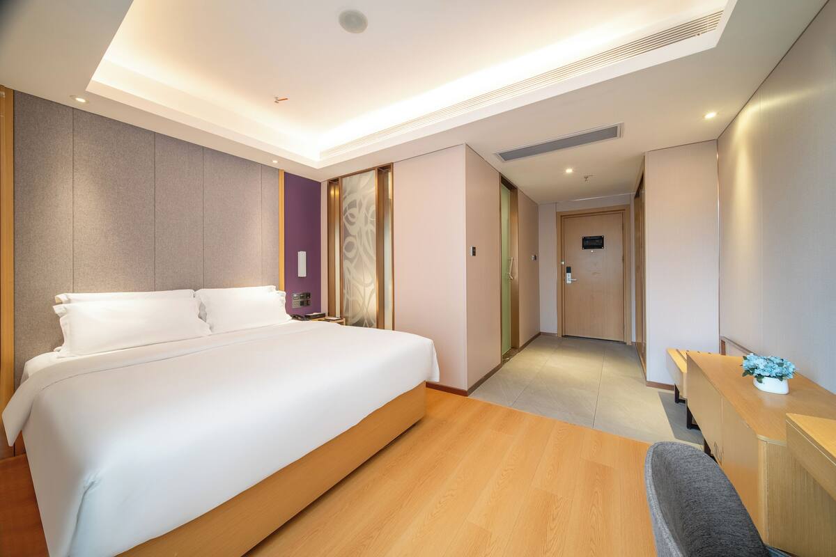 Quarto de hotel moderno com uma cama grande, piso de madeira, uma escrivaninha e um banco.