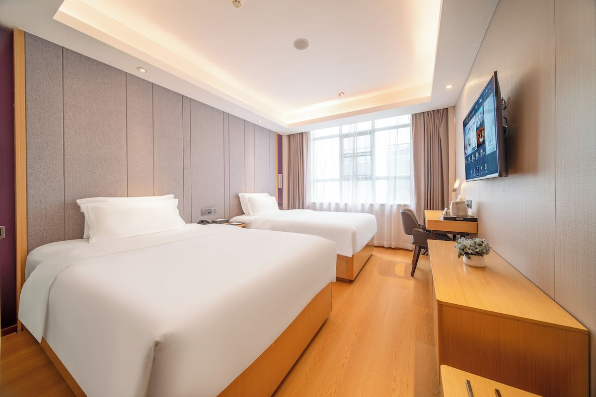 Quarto de hotel com duas camas, uma escrivaninha, televisão e janela com cortinas.