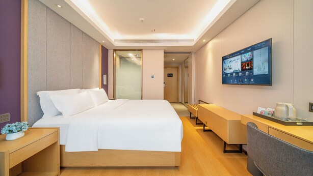 Habitación de hotel moderna con una cama grande, un escritorio, una silla y un televisor montado en la pared.